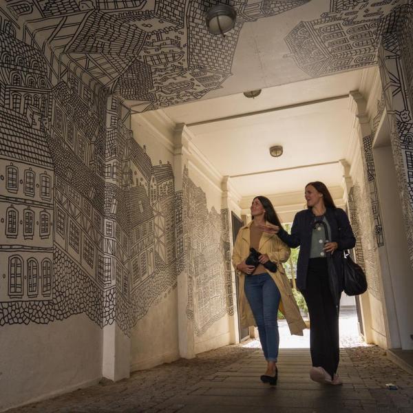 To voksne kvinder i regnvejr ser street art af Daniel Van der Noon i Destination Kystlandet.