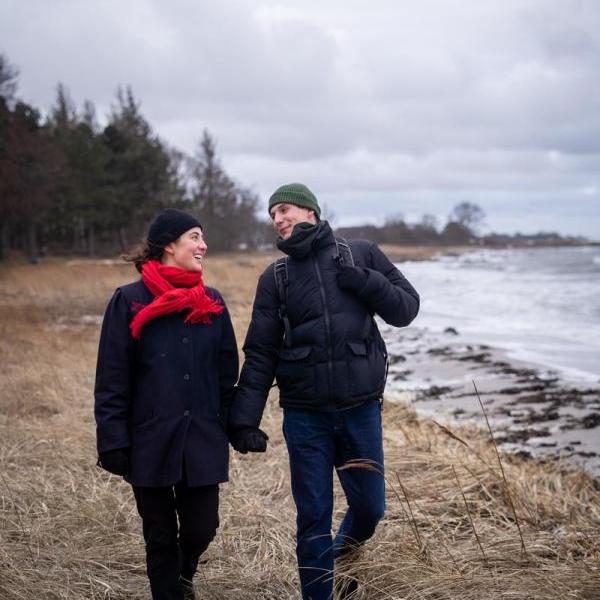 mand og kvinde går langs stranden en vinterdag med hue og  halstørklæde