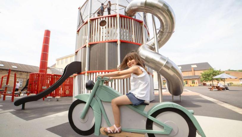 Pige sidder på vippe motorcykel på industrimuseets legeplads