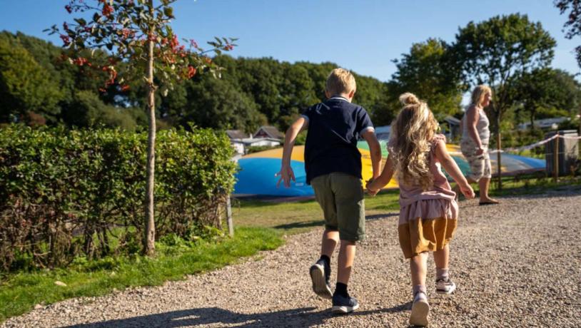 To børn med hinanden i hånden i fuld fart på vej hen mod hoppepuden på legepladsen på Horsens City Camping - en del af Destination Kystlandet