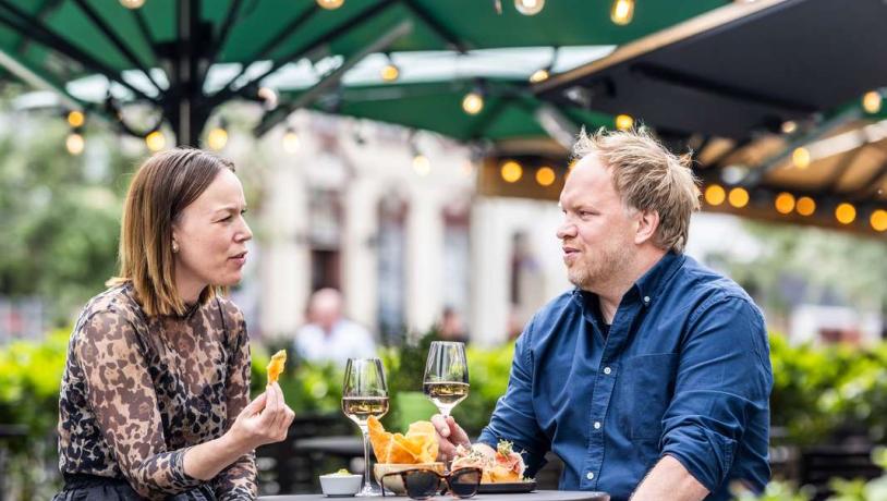 A man and a woman are sitting outside at a bar table under a green parasol