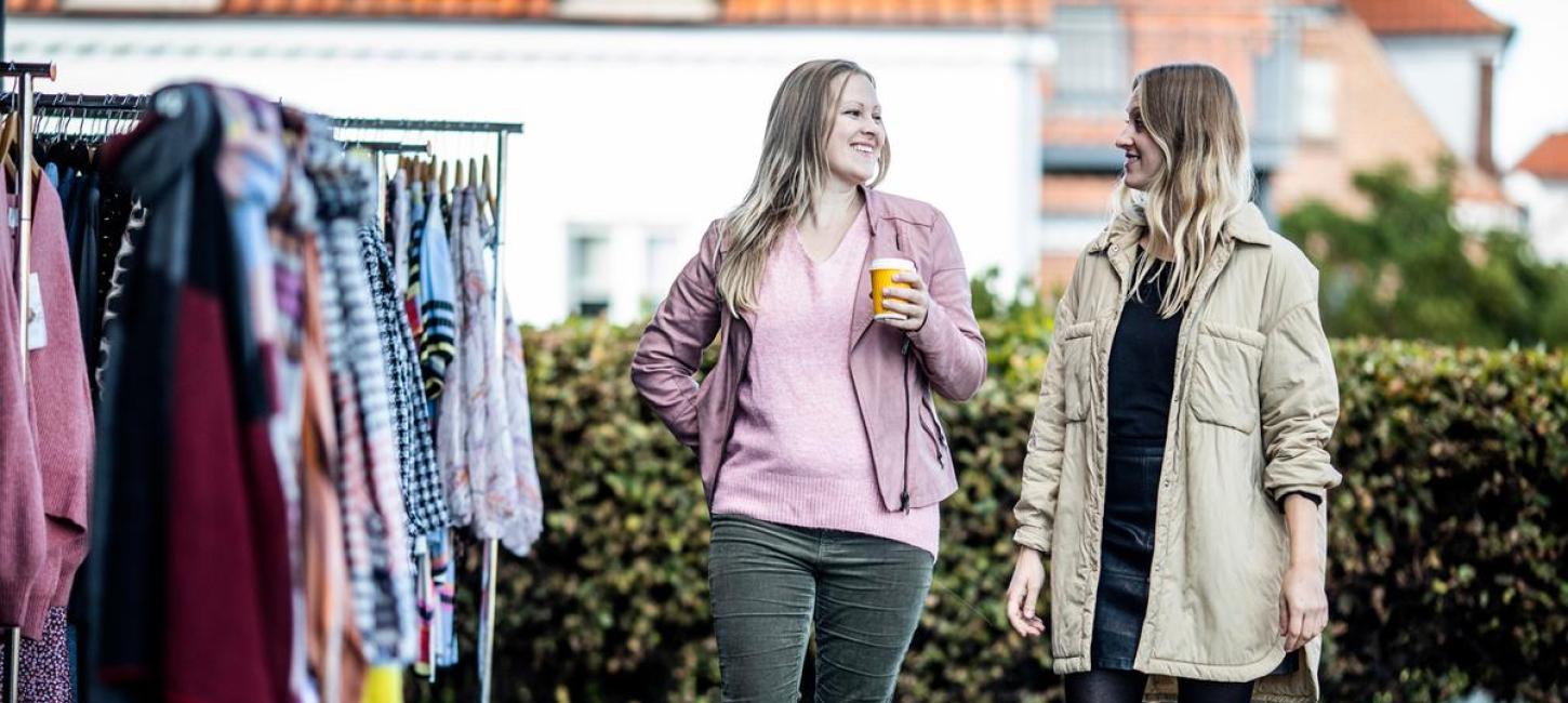Veninder går og taler ved siden af tøj stativer