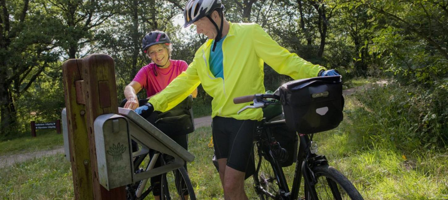 Ældre par på cykeltur kigger på skilt ved Gudenåens udspring