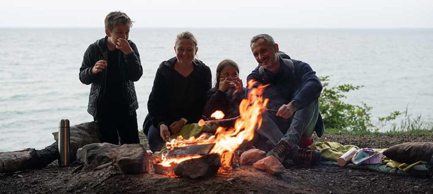 Familie sidder om et bål med havudsigt ved Staksrode Skov