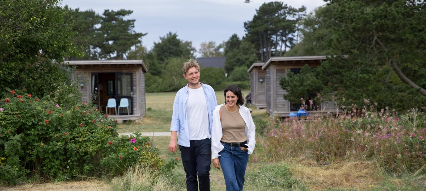 Par går mod stranden foran hytte på Tunø Teltplads i Destination Kystlandet