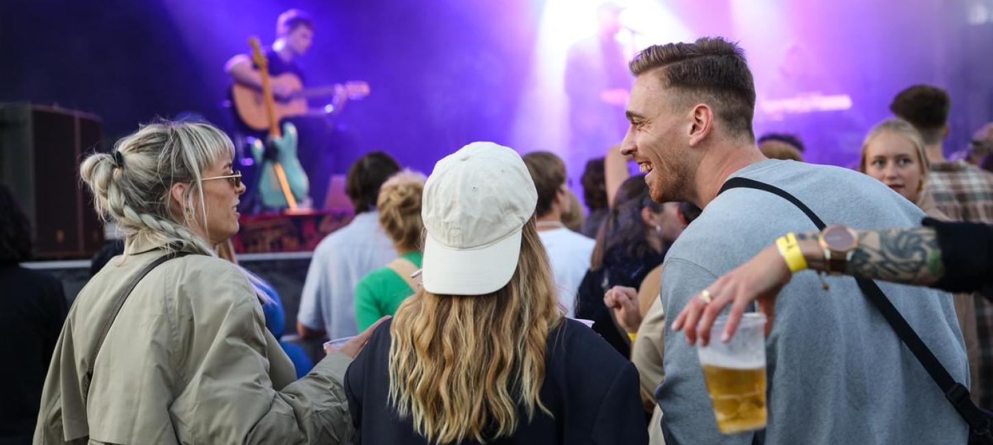 En mand og to kvinder i festivalstemning og koncert foran en stor scene på spillestedet Platform K i Horsens. 