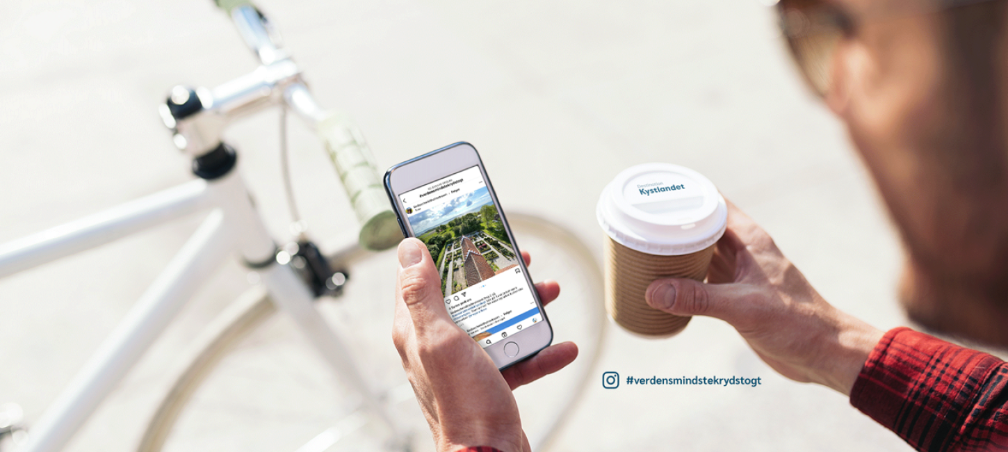 Mand kigger på mobil med Destination Kystlandet på skærmen og cykel og to-gokaffe
