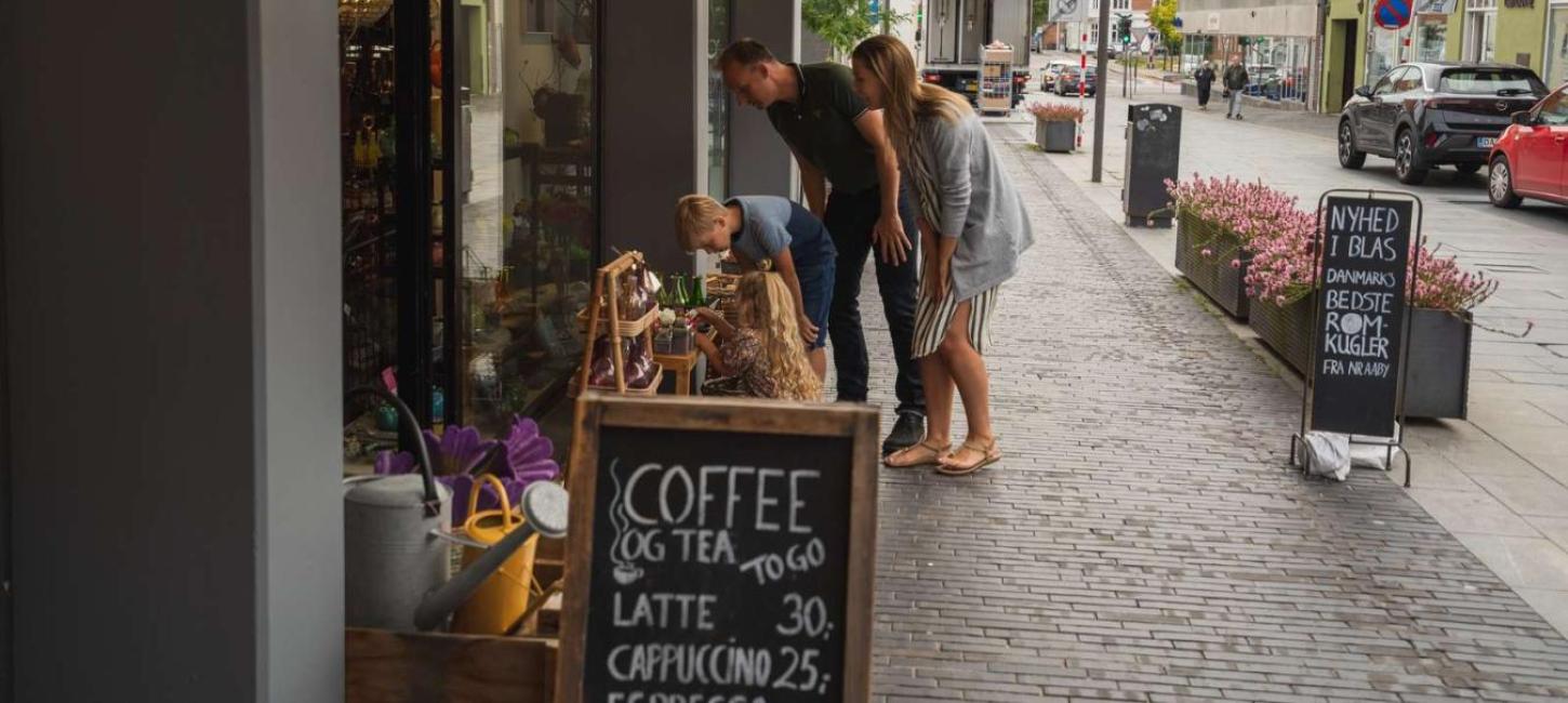 Familie på shopping kigger på varer uden for butik i Odder by - en del af Destination Kystlandet