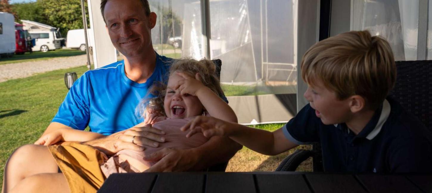 Far med to børn i fortelt ved campingvogn på Horsens City Camping - en del af Destination Kystlandet