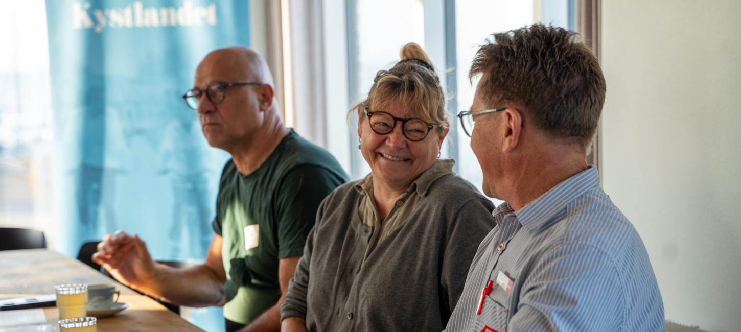 tre mennesker sidder på række ved et mødebord