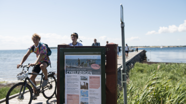 Cyklister på Alrø med skilt for cykelfærgen i forgrunden