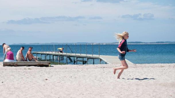 Pige løber hen ad Hou Strand ved Hou Strand Camping mens bedsteforældre kigger i baggrunden