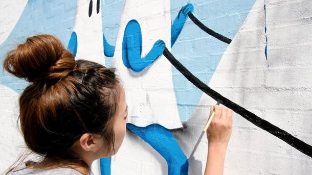 Kvindelig streetart kunstner maler et gavlmaleri i Horsens en del af Kystlandet
