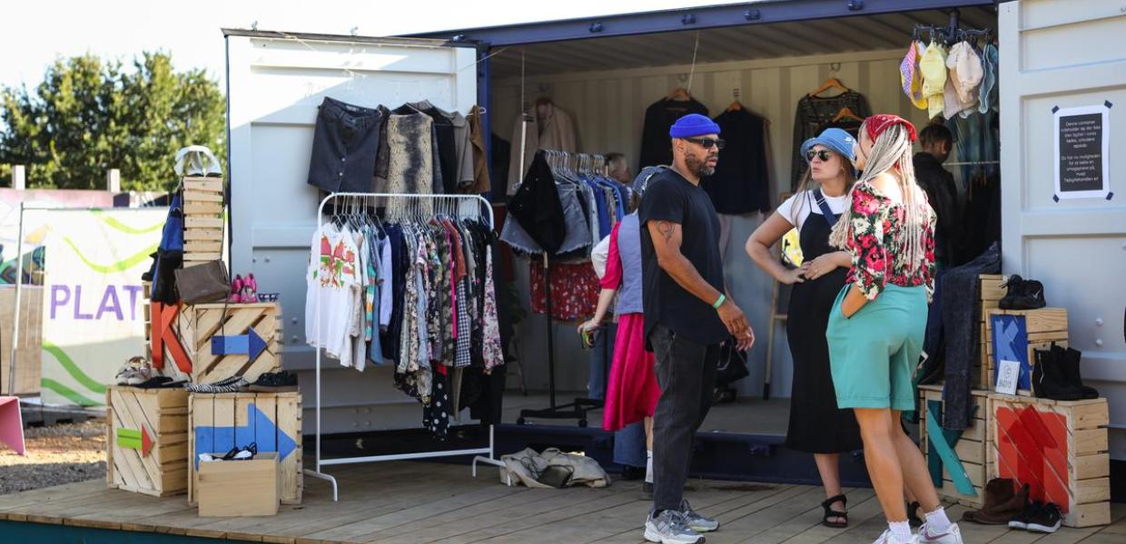 Gruppe af unge står ved en blå skibscontainer fyldt med tøj på tøjstativer ved Platform K  kulturhus i Horsens i Destination Kystlandet