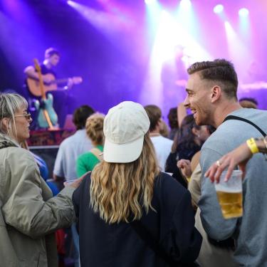 En mand og to kvinder i festivalstemning og koncert foran en stor scene på spillestedet Platform K i Horsens. 
