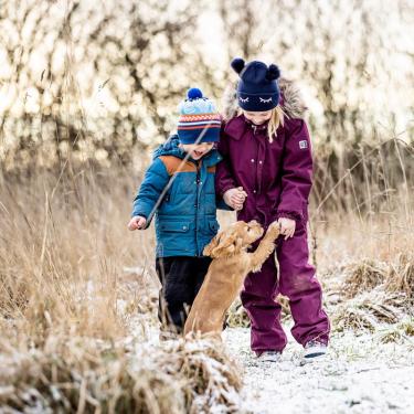 To børn leger med en hund i sne i Kystlandet