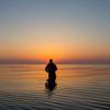 Mand fisker i havet ved solopgang