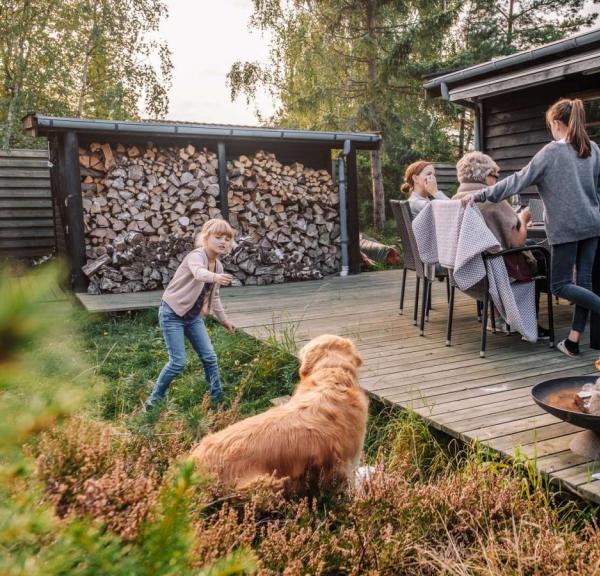 Familie hygger på terrassen i et feriehus i Kystlandet og pige leger med hund og ild i bålfad