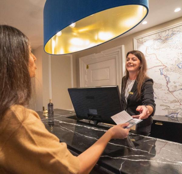 Kvinde tjekker ind på Jørgensens Hotel mens receptionist rækker hende nøglekort