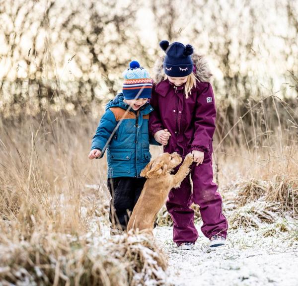 To børn leger med en hund i sne i Kystlandet