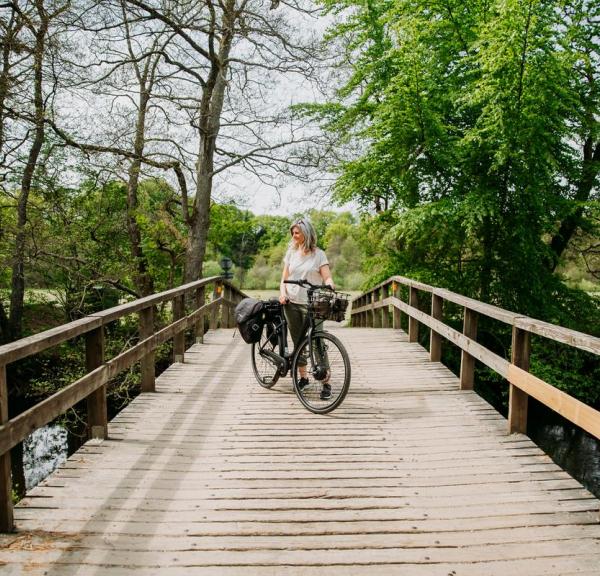 Kvinde står med en sort elcykel på en træbro ved Gudenåen nær Den Genfundne Bro