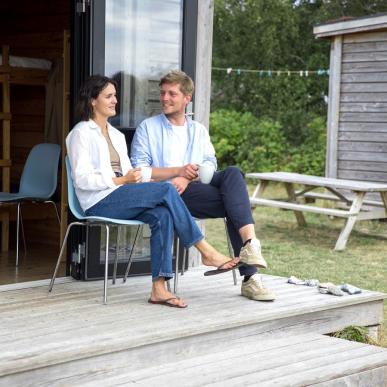 Par sidder og snakker foran hytte på Tunø Teltplads i Destination Kystlandet