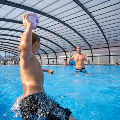 En dreng og en far spiller bold i en pool ved Horsens City Camping ved Husodde i Destination Kystlandet