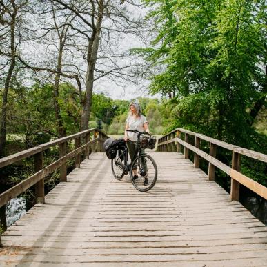 Kvinde står med en sort elcykel på en træbro ved Gudenåen nær Den Genfundne Bro