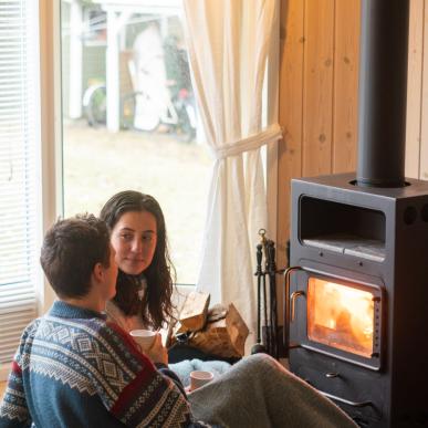 Mand og kvinde sidder foran en brændeovn i et sommerhus