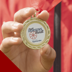 Barn i rød trøje fremviser medalje for skattejagten Horsens Rundt - en af fire skattejagter i Destination Kystlandet