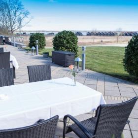 Udendørs terrasse med bord med hvid dug og stole ved Hotel Juelsminde Strand i Destination Kystlandet