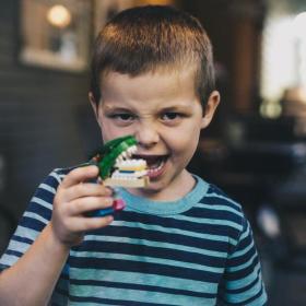Dreng laver sjovt ansigt mens han holder en legetøjsdinosaur 