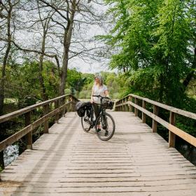 Kvinde står med en sort elcykel på en træbro ved Gudenåen nær Den Genfundne Bro
