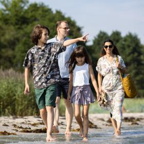 Familie med far mor og to børn går ved strand ved Odder 