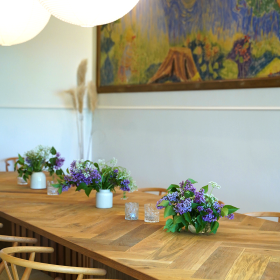 Bord i sildeparket med y-stole sat til og lilla syrener på bordet